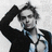Pixelated grayscale image of a person with one arm raised, wearing a dark jacket over a light shirt, with text reading "I Think I'm In Love <3" on black background.