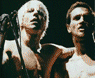 Two distinct band member images displayed in a with pixelated borders, one showing two individuals near microphones and the other three embracing