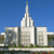 Pixelated static image of a tall white temple with a spire against a clear blue sky, surrounded by smaller buildings and greenery.