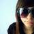 Pixelated close-up of a person with long brown hair wearing dark sunglasses and a black top against light blue background.