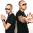 Two pixelated figures in black shirts with sunglasses, one holding a microphone and the other gesturing outward against white background.