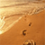 A pixelated beach scene with golden sand, a bright sunlit sky, and scattered dark brown footprints on the sand.