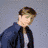 A pixelated image of a person with brown hair wearing a dark jacket over a light shirt against a gray background.