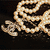 A coiled golden chain with a silver clasp on a dark background, partially obscured by a gray overlay in the bottom-right corner.