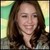 A static pixelated image of a person with long brown hair, closed eyes, and a slight smile against a blurred green and yellow background.