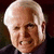 Static pixelated image of an elderly man with white hair, light skin tone, and a dark suit against a dark background.