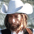 A pixelated figure wearing a white cowboy hat and dark clothing, with a light-colored background.