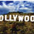 Pixelated static image showing large white text 'HOLLYWOOD' against a blurred background of blue sky and brown terrain.