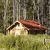 Pixelated image of a small house with a red roof and light-colored walls, set against a blurred forest background with tall trees and green grass.