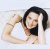 A pixelated image of a person with dark hair wearing a white sleeveless top, holding an object near their face against a light background.