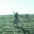 Pixelated figure in dark clothing stands on a greenish field with light sky background, holding an object above its head.