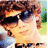 Pixelated image of a person with dark hair wearing sunglasses and a light-colored top, standing outdoors against greenery.