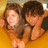 Two people with brown hair pose closely together against a warm-toned background with visible pixelation.