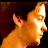 Pixelated static image of a person's profile with orange and brown tones against dark background, appearing to be a low-resolution digital portrait or stylized character depiction.