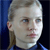 Pixelated close-up of a person with light hair tied back, wearing a dark blue top against a dark blue background.