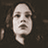 Pixelated static image of a person's face with dark hair against a brown background, rendered in low-resolution grayscale tones.