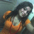 Pixelated image of a person with dark hair wearing an orange outfit, holding a light-colored object against a blurred background.