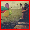 A person sits on a wooden pier by water, holding a string attached to colorful balloons, with a muted color palette and soft focus.