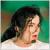 Pixelated image of a person with dark hair tied back, light skin, and a green background with brown horizontal bands.