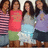 Four people stand side-by-side in a group pose, each wearing distinct casual clothing with visible colors and patterns.