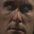 Pixelated close-up of a face with dark eyes, light skin, and a neutral expression against a brown background.