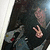 A person in dark clothing makes a peace sign with their right hand while holding a guitar, with a blurred background.