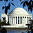 Static pixel art of a white domed building with columns against a blue sky, framed by dark tree silhouettes on both sides.