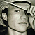 Static pixelated image of a person wearing a light-colored cap and dark clothing, with visible ear and neck details.