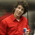 A person in a red collared shirt holds a blue and white object against a dark background.