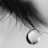 Black-and-white close-up of a teardrop on a cheek with red pixelated text on a black background.