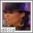 Alicia Keys wearing a black fedora and large earrings, singing into a microphone with a pink and purple background.