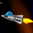 A silver spaceship with a blue cockpit glides through space, emitting a yellow-orange flame from its rear against a dark background with brown nebula-like streaks and scattered white stars.