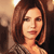Static pixelated image of a person with shoulder-length brown hair, closed eyes, and light skin tone wearing a patterned top against a warm-toned background.