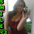 A pixelated image shows a person with long dark hair wearing a maroon top, holding hands near their face in front of greenery and a bright background.