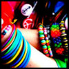 A colorful, pixelated image of a person with rainbow-striped hair and a red headband, wearing a white top and multiple beaded bracelets.