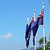 Pixelated image of a figure in dark blue clothing performing a high kick against a light blue sky background with faint clouds.