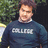 A pixelated image of a person wearing a dark blue sweater with white text, standing outdoors against green foliage and a dark background.