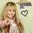 Pixelated image of a smiling woman with long light brown hair wearing a white top, with a purple and brown object and a black-and-white heart symbol on a light green background.