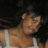 Pixelated static image of a person with light brown skin wearing a white sleeveless top against a dark background.