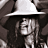 A pixelated grayscale image shows a figure wearing a wide-brimmed hat and long hair, with a partially obscured face and dark clothing against a muted background.