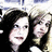 Two people with dark hair pose closely together against a light background, one wearing black clothing.