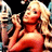 Pixelated static image of a person with light-colored hair wearing red clothing, holding an object near their face against a dark background.