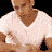 Pixelated static image of a person wearing a white V-neck shirt with brown skin tone and visible neck, cropped to show upper torso against black background.