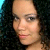Pixelated close-up of a person with dark curly hair against a dark background, showing light skin tone and pink lips.