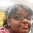 Pixelated close-up of a person with short dark hair, brown skin tone, and visible facial features including eyes, nose, mouth, and ears against a blurred background.