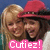 Two people with light brown hair and a person wearing a red cowboy hat stand close together, smiling under a pink banner reading "Cutiez!" in white pixelated text.