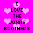 Pixelated text on a bright pink background with light pink heart shapes, displaying "I LOVE THE JONAS BROTHERS" in two vertical
