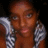 Pixelated close-up of a person with brown skin tone wearing a checkered shirt with white and dark gray squares, set against a dark background.
