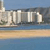 A pixelated landscape with a sandy beach, blue water, and a row of tall white buildings under a light blue sky.