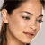 A pixelated close-up of a person's face with dark hair tied back, showing closed eyes and a neutral expression against a light background.